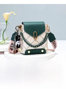 Detail of a quilted crossbody bag with green trim, gold chain, and teddy bear charm