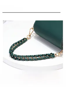 Detail of dark green bag with golden chain strap and metallic hook on white surface