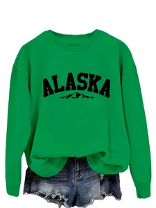 Close-up of green crewneck Alaska sweatshirt with mountain graphic and denim shorts
