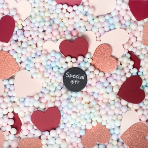 Special gift black round tag surrounded by colorful heart confetti and pastel foam beads
