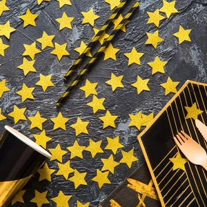 Confeti de estrellas doradas y vajilla de fiesta elegante negra y oro sobre fondo de piedra