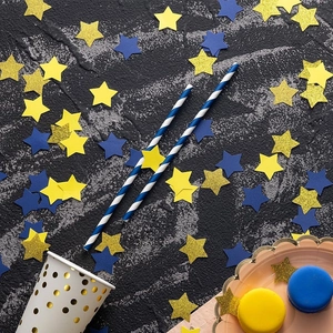 Primer plano de pajitas de papel a rayas azules y blancas con confeti de estrellas decorativas