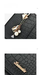 Detail of black crocodile pattern handbag featuring golden hardware and decorative charms