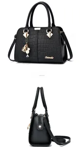 Detail of black faux crocodile leather handbag with gold metal logo and pearl floral charm