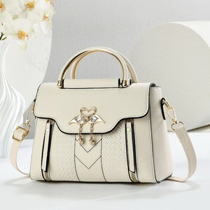 Detailed view of cream leather handbag with gold swan ornament and textured stitching