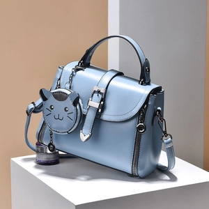 Light blue faux leather crossbody bag with a cute cat pendant on minimalist display