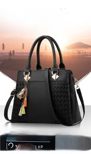 Détail du sac cabas en simili cuir noir avec texture tressée et pompon coloré sur la plage