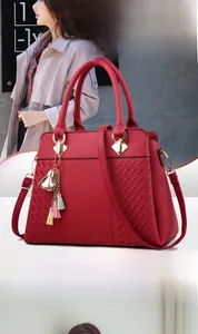 Détail du sac à main rouge texture litchi avec finitions dorées et pompon coloré