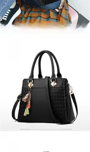 Détail du sac à main noir en simili cuir avec texture tressée et breloque à pompon métallique