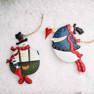 Pair of vintage tin snowman ornaments with red scarves on a white snowy background