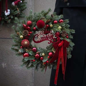 Detail of Christmas wreath with red ornaments, natural pine cones, and a Merry Christmas sign