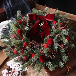 Detailed view of Christmas wreath featuring red velvet bows, pine cones, and gold deer charm