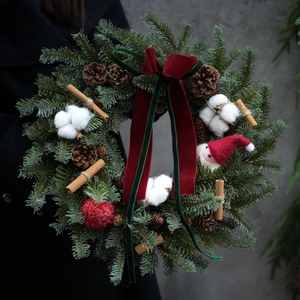 Christmas wreath with pine cones cotton and red velvet bow held by a person