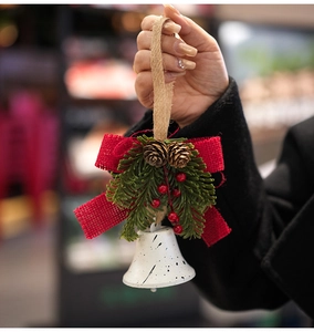 Close-up of a white bell pendant with a red plaid bow, pine needles, and natural pinecone