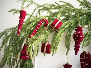 Adornos navideños de terciopelo rojo con purpurina dorada colgados en ramas de pino verde