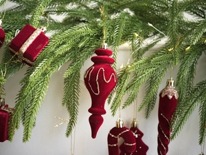 Primer plano de adornos navideños rojos con purpurina dorada sobre ramas de pino verde