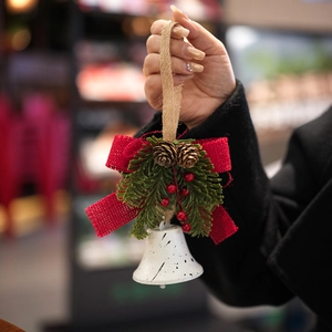 Christmas bell ornament with red bow, pine cones, and berries held in hand