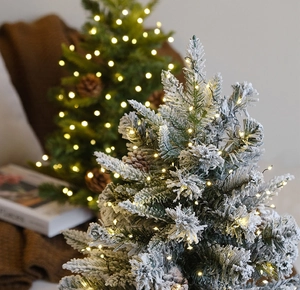 Détail de mini sapins de Noël enneigés avec lumières LED chaudes et pommes de pin