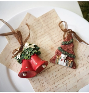 Detalle de adornos navideños de resina con campanas, osito de peluche y cintas marrones