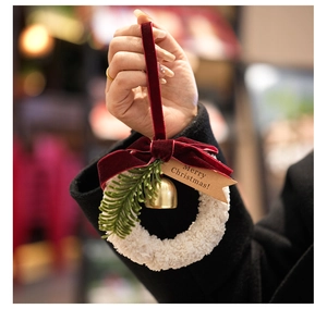 Close-up of Christmas wreath ornament with gold bell, red velvet bow, and holiday tag