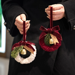 Pair of plush Christmas wreaths with velvet bows and golden bells on black background