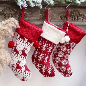 Drie rood-witte gebreide kerstsokken met rendier- en sneeuwvlokpatronen hangend aan de muur