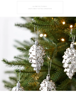 Silver pine cone Christmas ornament with shiny finish hanging on a lit Xmas tree