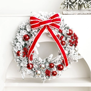 Flocked Christmas wreath with large red bow and ornaments on a white arch display