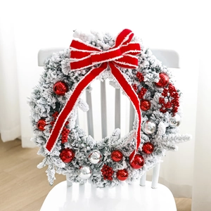 White flocked Christmas wreath with red ornaments and a velvet bow on a wooden chair