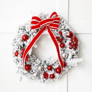 Flocked Christmas wreath with red bow and ornaments on white background for door decor