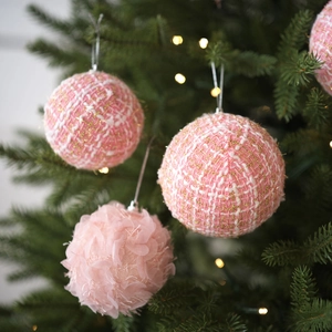 Pink plush woven Christmas balls with gold thread hanging on a festive green tree