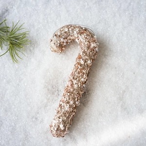 Detail of rose gold candy cane ornament with sequins and pearls on white snow background