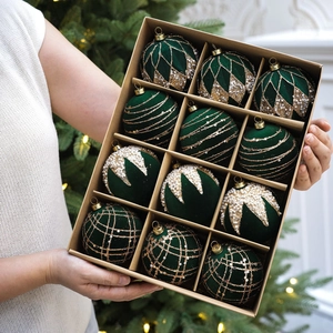 Mains tenant un lot de 12 boules de Noël en velours vert foncé avec paillettes dorées