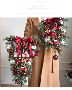 Close-up of burgundy bow and Santa Claus holiday ornament on a green Christmas door swag