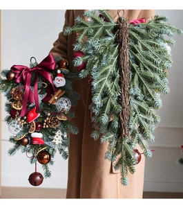 Detail of Christmas wreath with Santa doll, red bow and pine cones held by hand