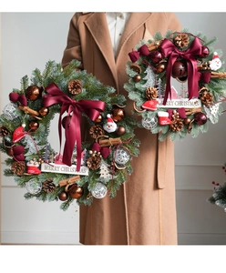 Close-up of a Christmas wreath with pine cones, red bows, and Merry Christmas sign