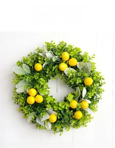 Close-up of artificial lemon wreath with lush green leaves on white wooden background