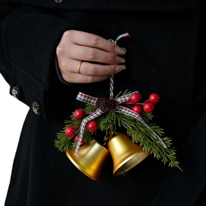 Christmas tree bells decoration with red berries and plaid bow held against dark coat