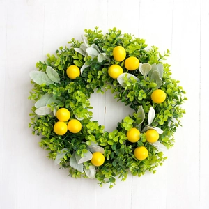 Artificial lemon wreath with green leaves and yellow fruit on white wood background