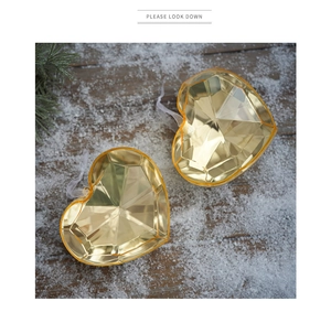 Close-up of golden faceted acrylic heart ornaments with ribbons on a snowy wooden background