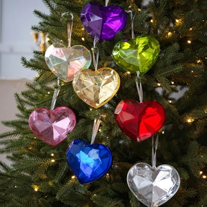Colorful faceted acrylic heart ornaments hanging on a Christmas tree with festive lights