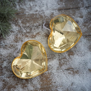 Set of two heart shaped acrylic ornaments with gemstone facets on snowy wood background