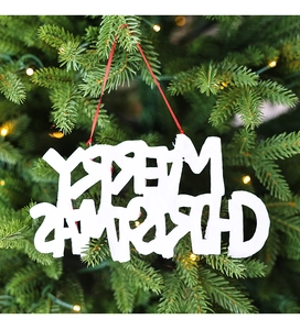 Close-up of white Merry Christmas letter ornament with snow texture on festive pine tree
