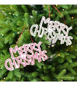 Detail of red and green Merry Christmas clay ornaments hanging on a festive lighted tree