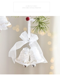 Nahaufnahme weißer gefrosteter Weihnachtsglocken mit Organzaschleife an einem Tannenzweig