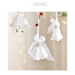 Weihnachtsglocke aus weißer Keramik mit Organza-Schleife an festlichen Kiefernzweigen