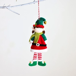 Bambola elfo di Natale con cappello verde e vestito rosso appesa a un ramo invernale