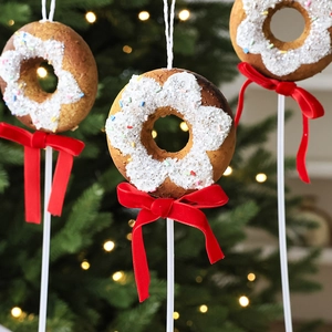 Trois ornements de Noël en forme de donut avec nœuds rouges devant un sapin festif