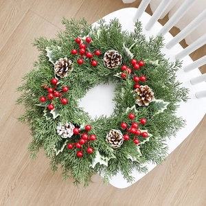Couronne de Noël avec baies rouges et pommes de pin posée sur une chaise blanche