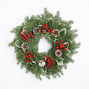 Couronne de Noël aux baies rouges et pommes de pin enneigées sur fond de bois blanc